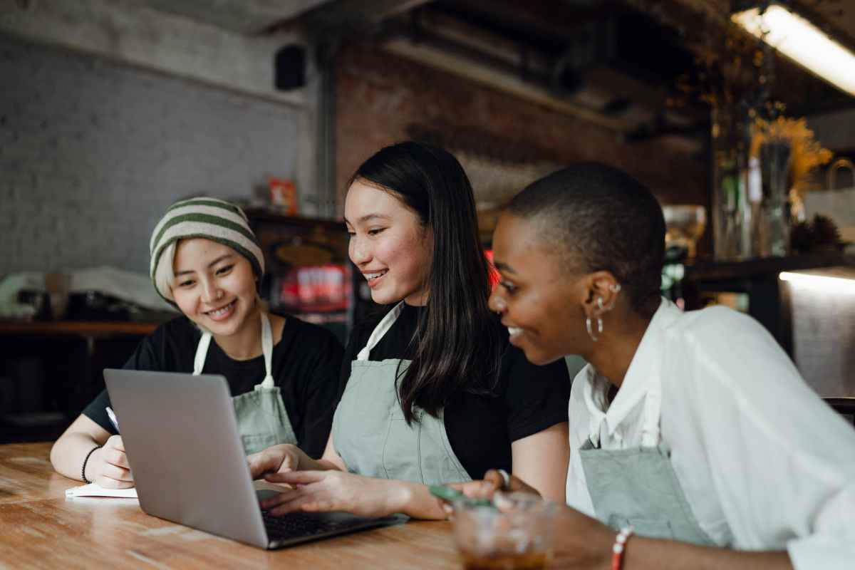 cheerful female colleagues working on laptop together in cafe