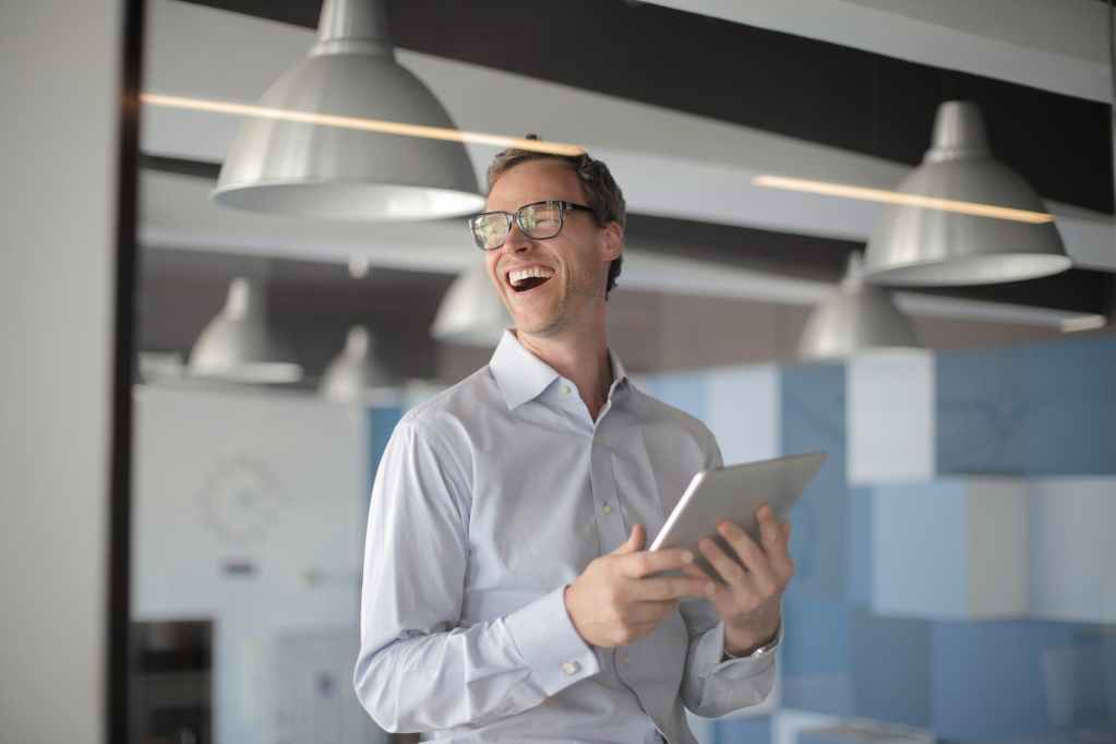 photo of laughing man in white dress shirt carrying a tablet